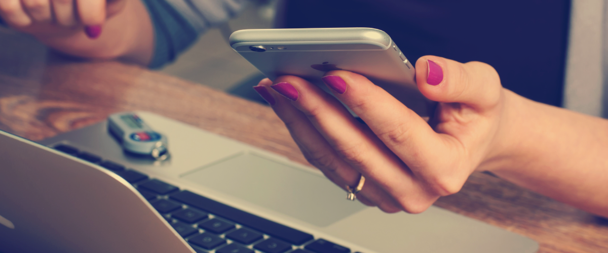 woman holding cell phone with laptop in front of her